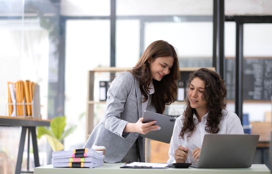 Two young Asian business woman talk, consult, discuss working with new startup project idea presentation analyze plan marketing and investment in the office..