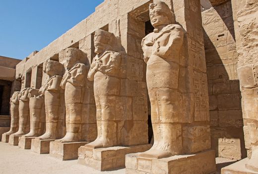 Large statues of Ramses III in ancient egyptian Karnak Temple with columns in courtyard area
