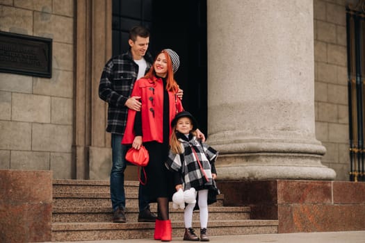 A stylish family of three strolls through the autumn city posing for a photographer . Dad, mom and daughter in the autumn city.