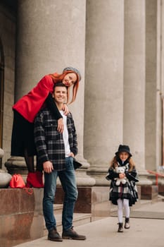 A stylish family of three strolls through the autumn city posing for a photographer . Dad, mom and daughter in the autumn city.