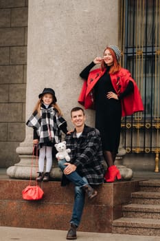 A stylish family of three strolls through the autumn city posing for a photographer . Dad, mom and daughter in the autumn city.