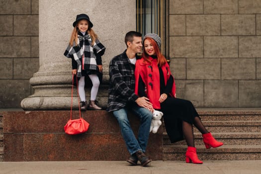 A stylish family of three strolls through the autumn city posing for a photographer . Dad, mom and daughter in the autumn city.