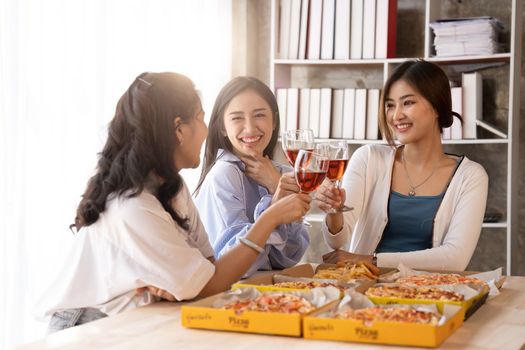 Group of Asian friends gather to celebrate Christmas with champagne and eating pizza at home. Joy of holiday party with friends or colleague concept