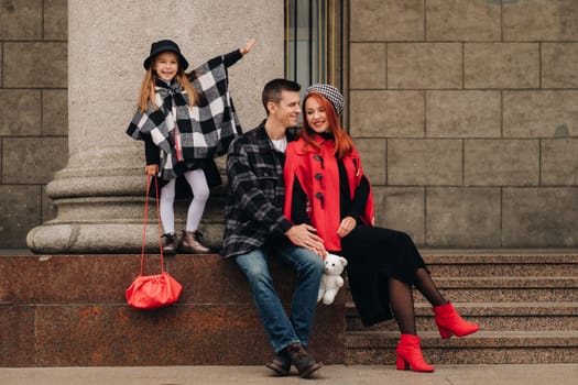 A stylish family of three strolls through the autumn city posing for a photographer . Dad, mom and daughter in the autumn city.