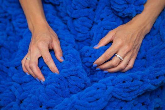 A girl wrapped in a large blue merino wool hand knitted blanket, a warm and very soft blanket, the girl enjoys the softness of the blanket