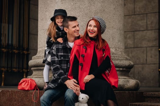 A stylish family of three strolls through the autumn city posing for a photographer . Dad, mom and daughter in the autumn city.