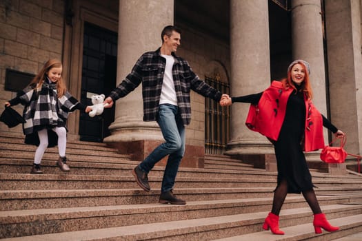 A stylish family of three strolls through the autumn city posing for a photographer . Dad, mom and daughter in the autumn city.