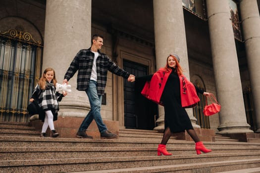 A stylish family of three strolls through the autumn city posing for a photographer . Dad, mom and daughter in the autumn city.