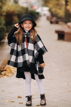 A stylish little girl in a hat walks around the autumn city.