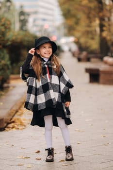 A stylish little girl in a hat walks around the autumn city.