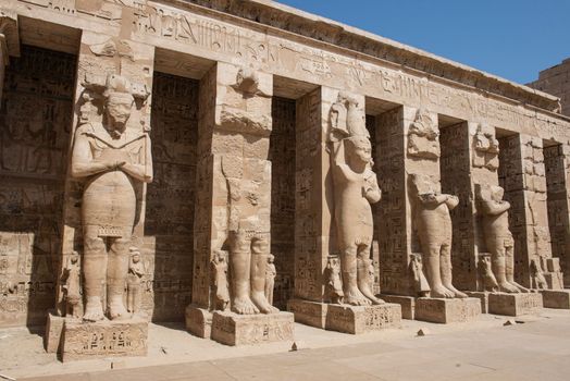 Large statues of Ramses II in ancient egyptian Medinat Habu Temple with columns in courtyard area