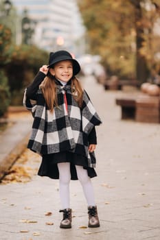 A stylish little girl in a hat walks around the autumn city.