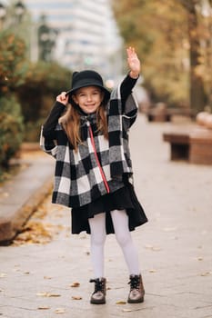 A stylish little girl in a hat walks around the autumn city.