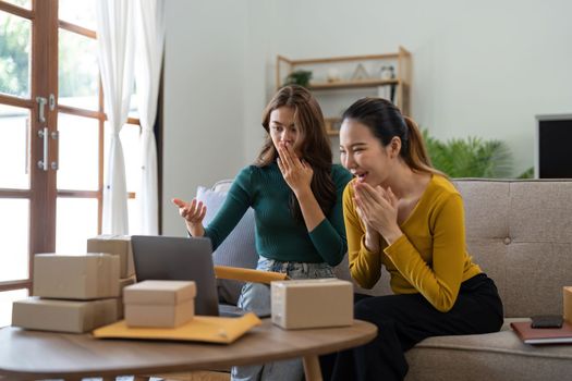 Two Young Asian women are happy and excited after a new order from SME customer, commercial checking, online marketing, Entrepreneur packing boxes, SME sellers, and freelance online sales concept.