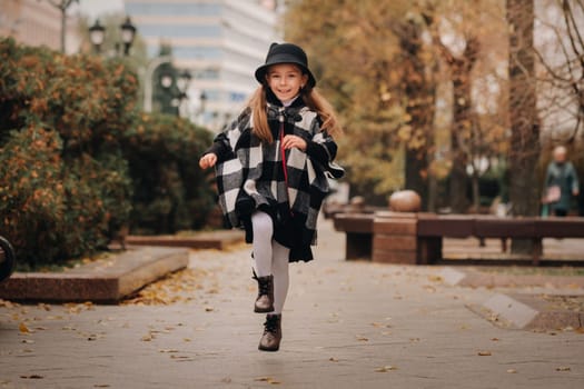 A stylish little girl in a hat walks around the autumn city.