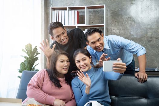 Friends watch sports on TV, cheer and celebrate. Happy diverse asian friend supporters fans sit on couch with popcorn and drinks. video call on mobile phone.