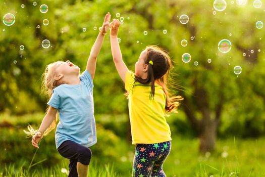 Two little girls are blowing soap bubbles, outdoor shoot