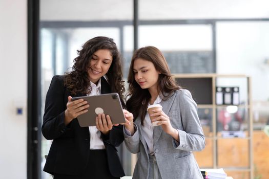 Two beautiful Asian businesswomen standing using digital tablet consulting and analyzing information in office work..