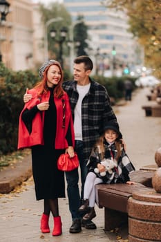 A stylish family of three strolls through the autumn city posing for a photographer . Dad, mom and daughter in the autumn city.