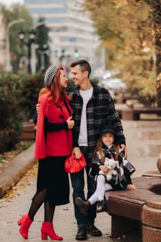 A stylish family of three strolls through the autumn city posing for a photographer . Dad, mom and daughter in the autumn city.