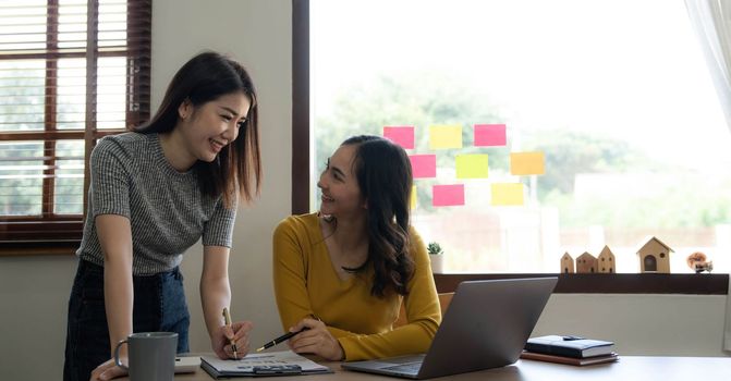 Two young Asian business woman talk, consult, discuss working with new startup project idea presentation analyze plan marketing and investment in the office...