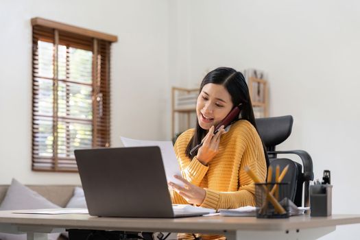 Asian woman talking on the phone and working with laptop calculator document on an office desk, planning analyzing the financial report, business plan investment, finance analysis concept