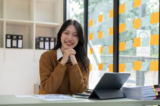 Portrait of Young beautiful Asian businesswoman sitting and smiling while working on laptop, Looking at camera.