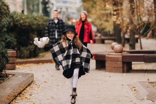 A little girl with her parents runs to the autumn city.A stylish family of three strolls through the autumn city,