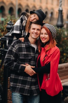 A stylish family of three strolls through the autumn city posing for a photographer . Dad, mom and daughter in the autumn city.