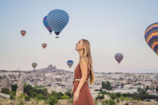 Tourist woman looking at hot air balloons in Cappadocia, Turkey. Happy Travel in Turkey concept. Woman on a mountain top enjoying wonderful view.
