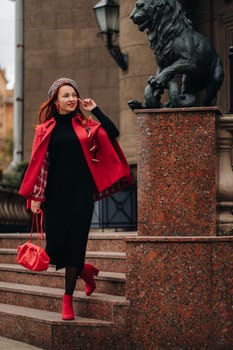 A beautiful stylish woman dressed in an elegant red coat with a stylish red handbag in the autumn city.