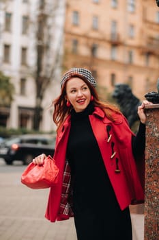 A beautiful stylish woman dressed in an elegant red coat with a stylish red handbag in the autumn city.