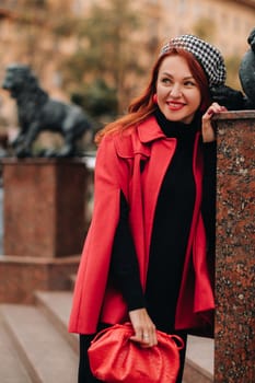 A beautiful stylish woman dressed in an elegant red coat with a stylish red handbag in the autumn city.