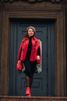 A beautiful stylish woman dressed in an elegant red coat with a stylish red handbag in the autumn city.