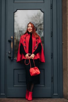 A beautiful stylish woman dressed in an elegant red coat with a stylish red handbag in the autumn city.