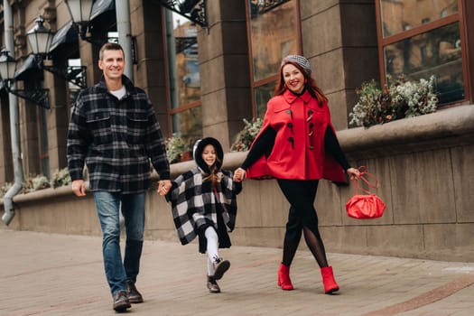 A stylish family of three walks in the city in autumn holding hands.