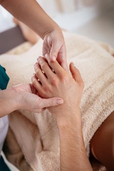 Close-up of a hads of young female therapist massaging young man's hand at beauty salon.  