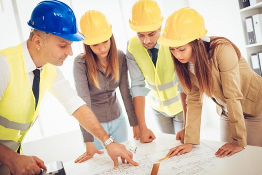 Successful young architects team with helmets on their heads, discussing construction plans and planning what to change to be better. They are in the office.