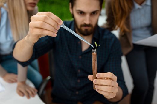 Close-up of a university biologist analysing the sample of plant in the lab tube, watering it with drops of nutritious fluid. Selective focus, focus on test tube, on foreground.