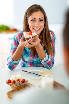 Portrait of a beautiful young woman who is eating healthy sandwich for the breakfast in the domestic kitchen. 