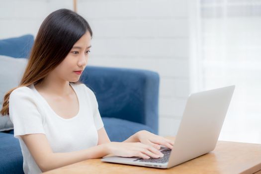 Beautiful young asian woman typing keyboard on laptop computer on desk at home, business woman working to internet online, freelance girl using notebook on table, communication and lifestyle concept.