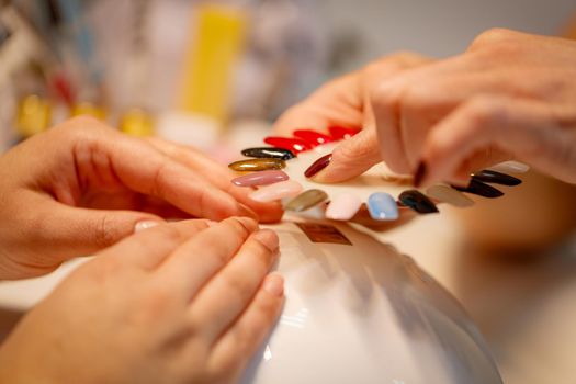 Close-up of a beautician and female clients hands holding samples and choosing colours nails at the beauty salon.