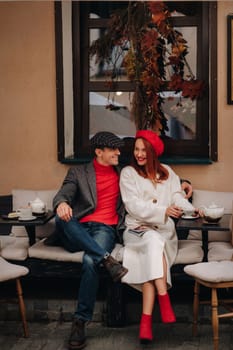 A happy stylish couple drinks coffee and smiles while sitting in a cafe on the street.