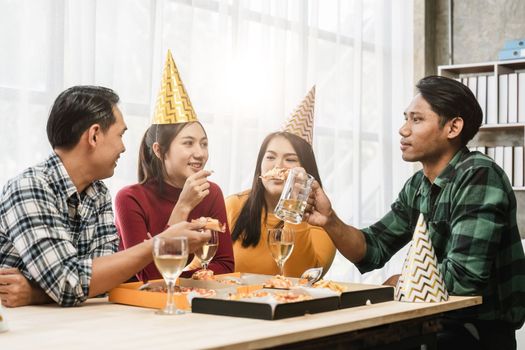 Group of diverse Asian friends gather to celebrate Christmas with champagne and eating pizza at home. Joy of holiday party with friends or colleague concept.
