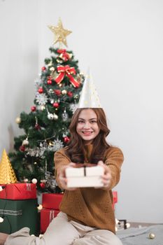 Portrait smiling girl hold gift box sit on floor in house indoors with x-mas christmas decoration.