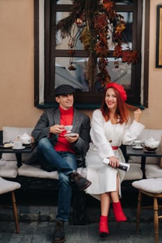 A happy stylish couple drinks coffee and smiles while sitting in a cafe on the street.