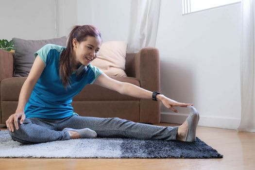 Smiling Asian woman doing yoga shoulder stretching online class at home in living room. Self isolation and workout at home during COVID-19..