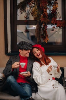 A happy stylish couple drinks coffee and smiles while sitting in a cafe on the street.