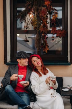 A happy stylish couple drinks coffee and smiles while sitting in a cafe on the street.