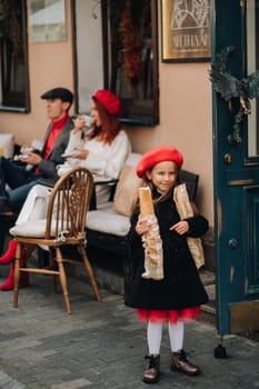 A stylish girl with baguettes stands near the store against the background of her parents.